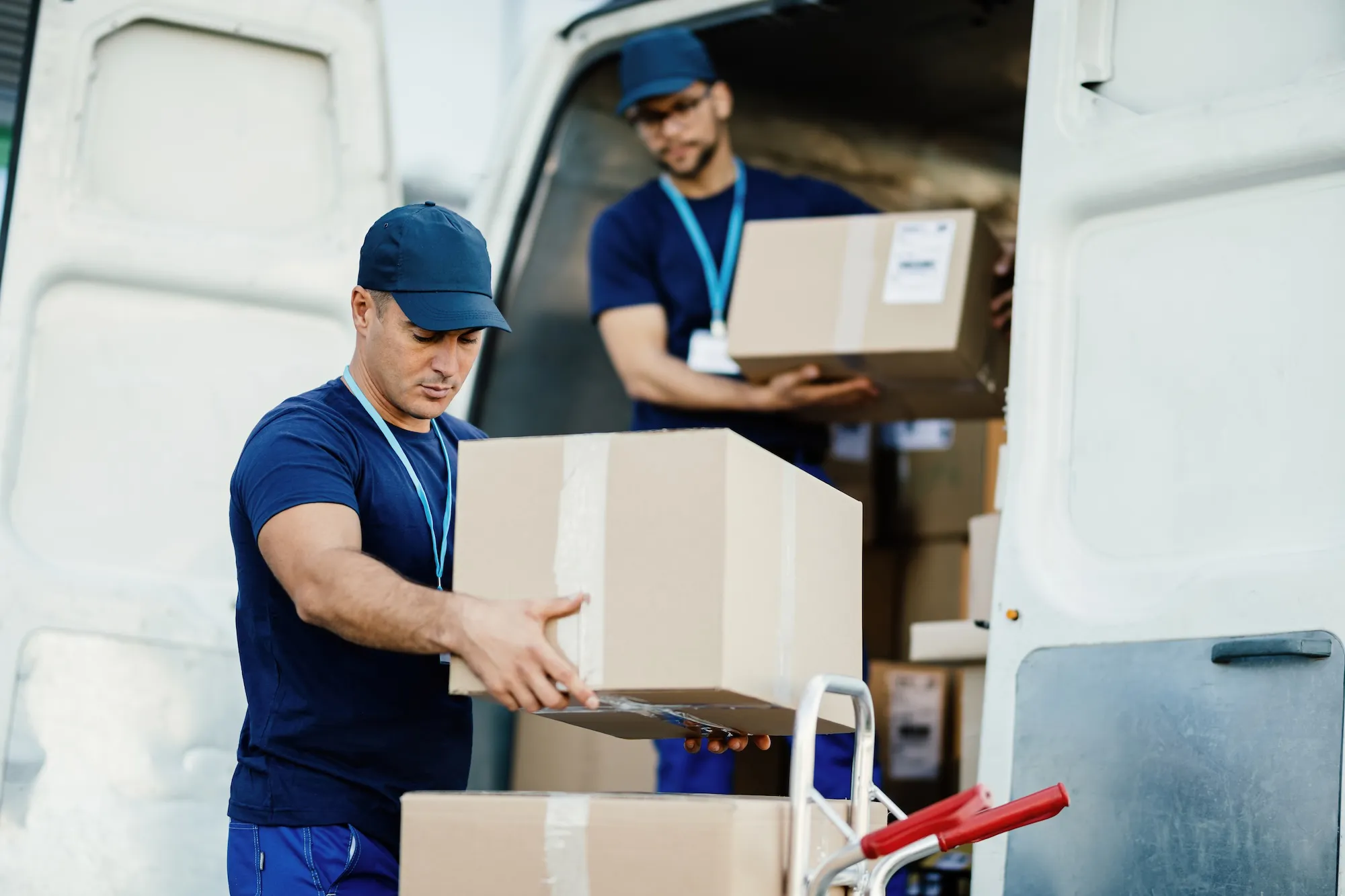 young-courier-his-colleague-unloading-cardboard-boxes-from-delivery-van young-courier-his-colleague-unloading-cardboard-boxes-from-delivery-van